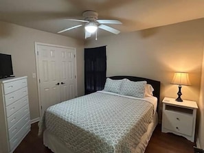 Un dormitorio con cama, mesita de noche, cómoda, ventilador de techo y una puerta.