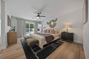 Ein modernes Schlafzimmer mit Bett, Nachttischen, Schreibtisch, Deckenventilator und Blick ins Freie.