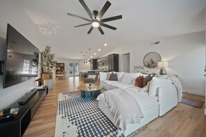Ein modernes Wohnzimmer mit Flachbildfernseher, Deckenventilator, Sofa und Essbereich.