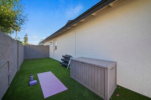 Ein Garten mit künstlichem Rasen, einer Holzterrasse und Fitnessgeräten.