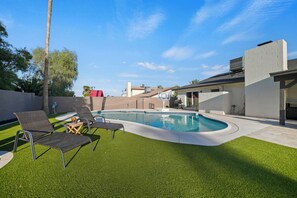 Ein Garten mit Schwimmbad, Kunstgrasanlage und Liegestühlen.
