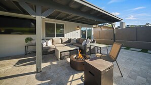 A covered patio area with a fire pit, outdoor furniture, and a view of the surrounding landscape. - Desert Retreat with Pool & Mountain Views (Phoenix)