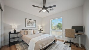 A bedroom with a bed, bedside tables, a desk with a chair, a ceiling fan, a window with blinds, and a framed artwork on the wall. - Desert Retreat with Pool & Mountain Views (Phoenix)