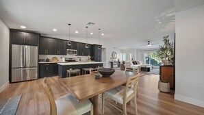 A modern kitchen with dark cabinetry, stainless steel appliances, pendant lighting, and a dining area with a wooden table and chairs. - Desert Retreat with Pool & Mountain Views (Phoenix)