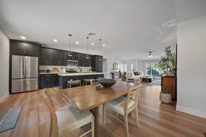 A modern kitchen with dark cabinetry, stainless steel appliances, pendant lighting, and a dining area with a wooden table and chairs. - Desert Retreat with Pool & Mountain Views (Phoenix)