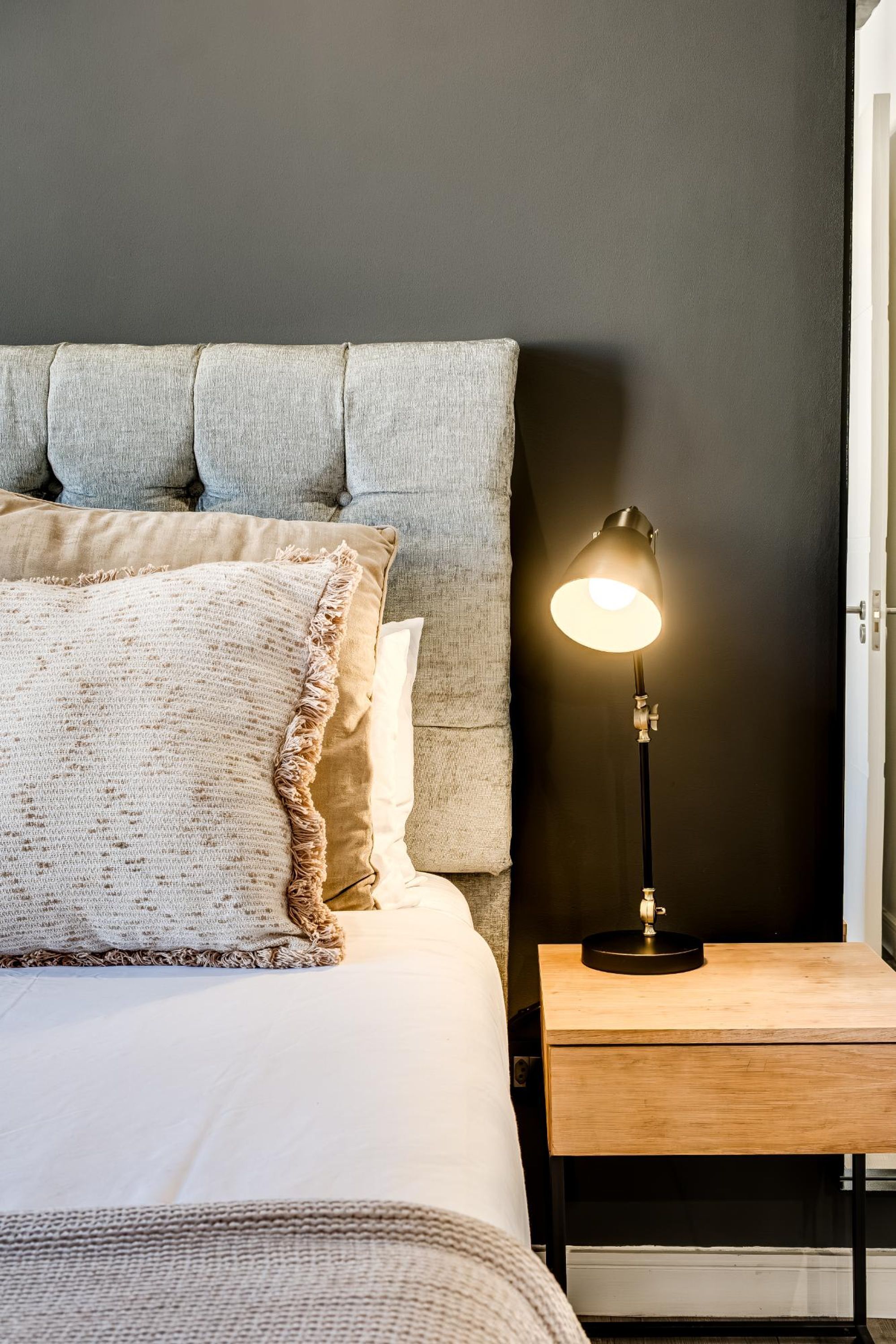 A neatly made bed with a headboard, a bedside lamp, and a wooden nightstand.