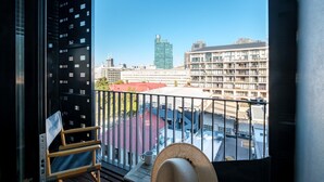 En balkon med udsigt over bybilledet, inklusive en høj bygning og en parkeringsplads.