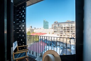Ein Balkon mit Blick auf eine Stadtlandschaft, darunter ein hohes Gebäude und ein Parkplatz.