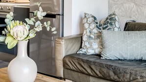 Et moderne køkken med rustfrie stålgrebe, et spiseområde med et træbord og en stue med sofa og dekorative puder.