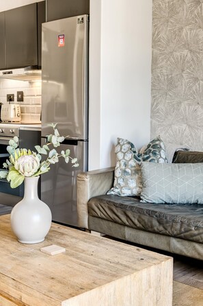 Eine moderne Küche mit Edelstahlgeräten, ein Essbereich mit Holztisch und ein Wohnzimmer mit Sofa und dekorativen Kissen.