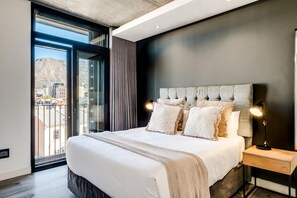 Ein modernes Schlafzimmer mit einem großen Bett, einem Nachttisch und Blick auf die Stadt durch ein großes Fenster.