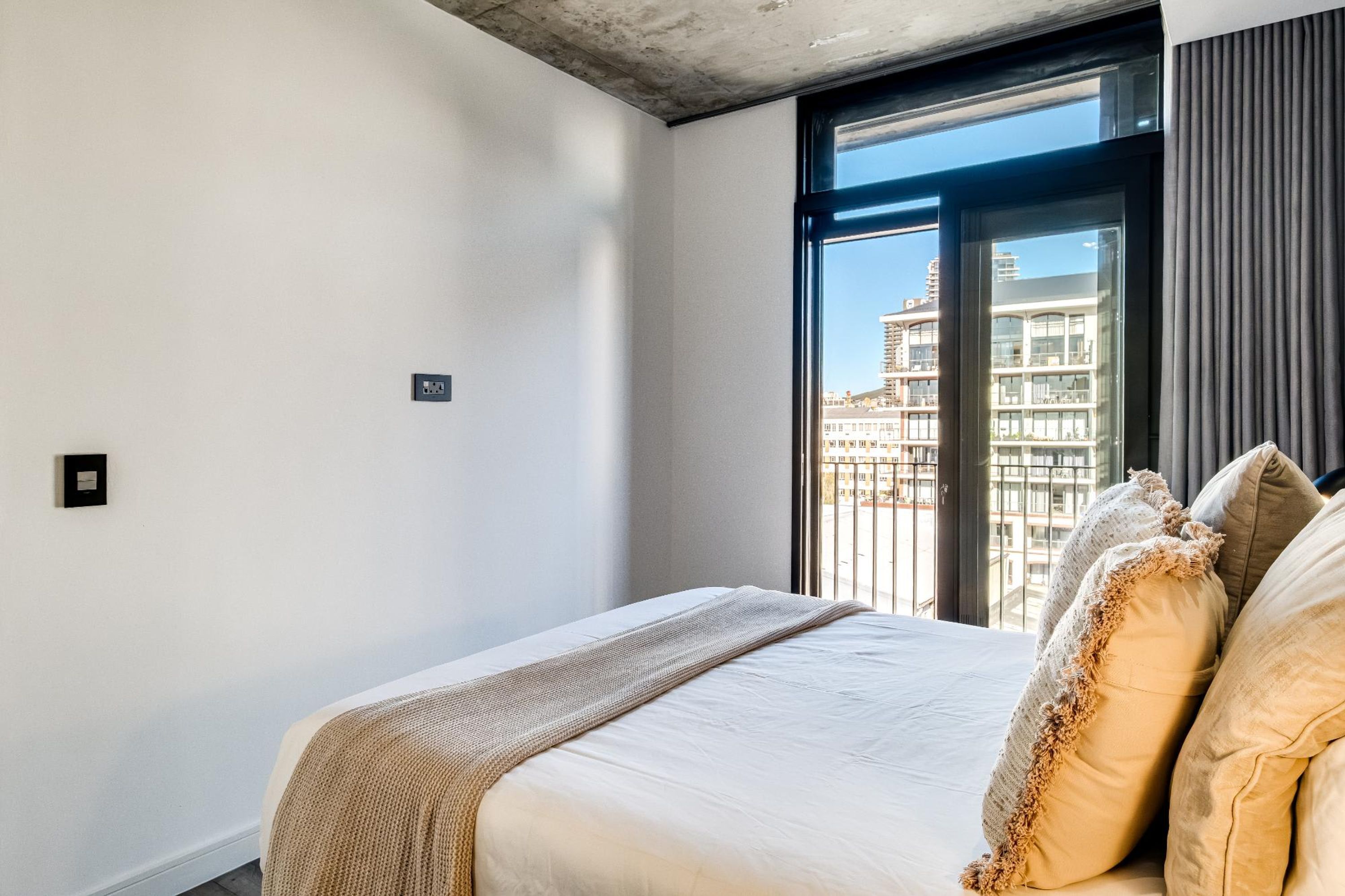 Una camera d'albergo con un letto grande, vista sui palazzi dalla finestra e una presa elettrica sulla parete.