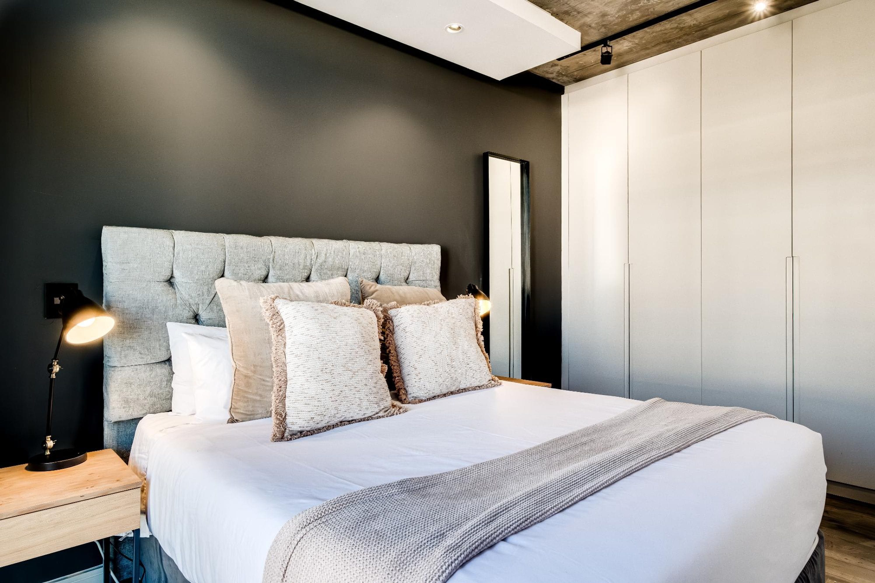 Een slaapkamer met een groot bed, een nachtkastje, een lamp en een kledingkast.