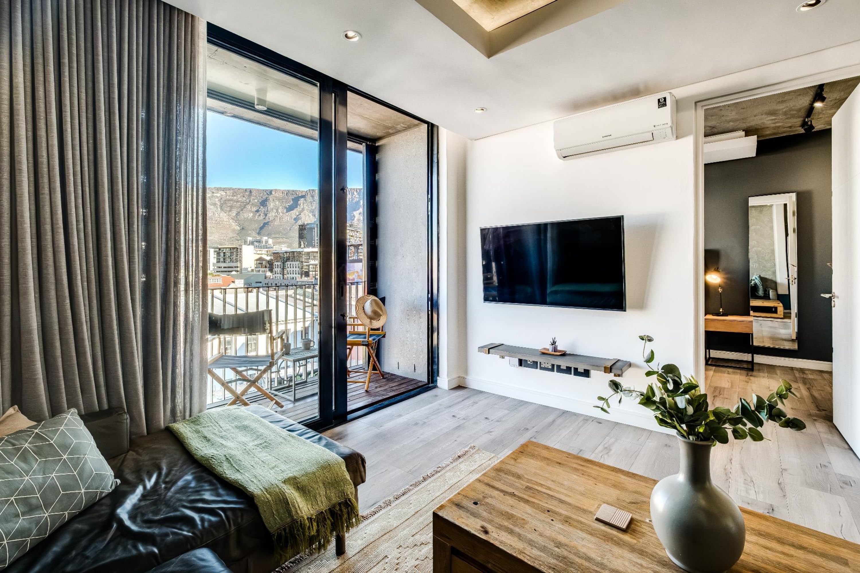 A modern living room with a large TV, a sofa, and a view of a cityscape through a sliding glass door.