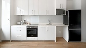 A modern kitchen with white cabinetry, a Bosch oven, a black refrigerator, and a microwave. - Stylish | Roof Top Pool | Studio Apartment | The Tokyo (Cape Town)
