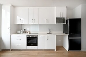 A modern kitchen with white cabinetry, a Bosch oven, a black refrigerator, and a microwave. - Stylish | Roof Top Pool | Studio Apartment | The Tokyo (Cape Town)