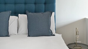 A bed with a tufted headboard, white and grey pillows, and a bedside table with a lamp. - Stylish | Roof Top Pool | Studio Apartment | The Tokyo (Cape Town)