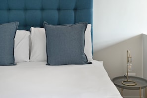A bed with a tufted headboard, white and grey pillows, and a bedside table with a lamp. - Stylish | Roof Top Pool | Studio Apartment | The Tokyo (Cape Town)