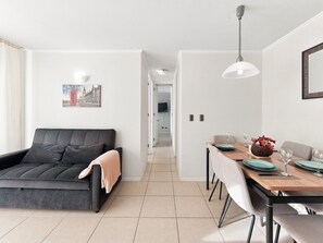 Ein modernes Wohnzimmer mit einer Couch, einem Esstisch für zwei Personen und einem Flur, der in einen anderen Raum führt.