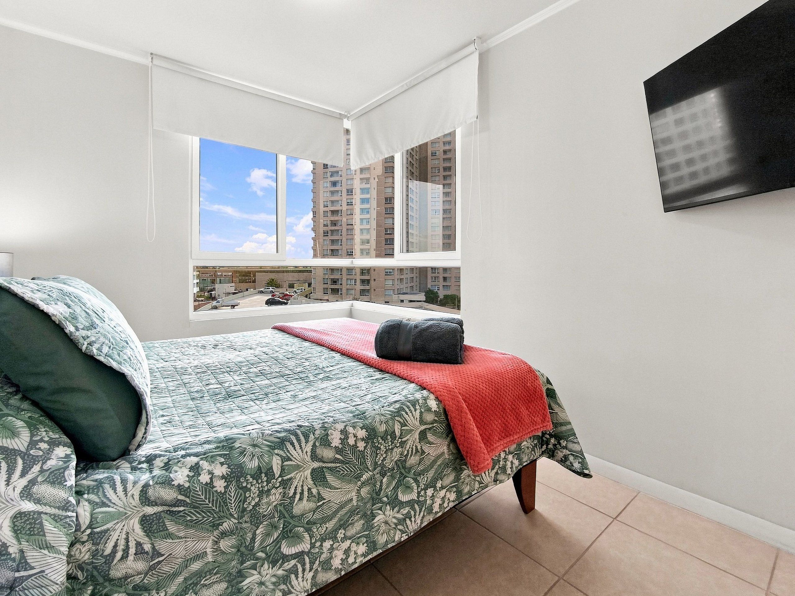 A bedroom with a bed, a window, and a view of a building.