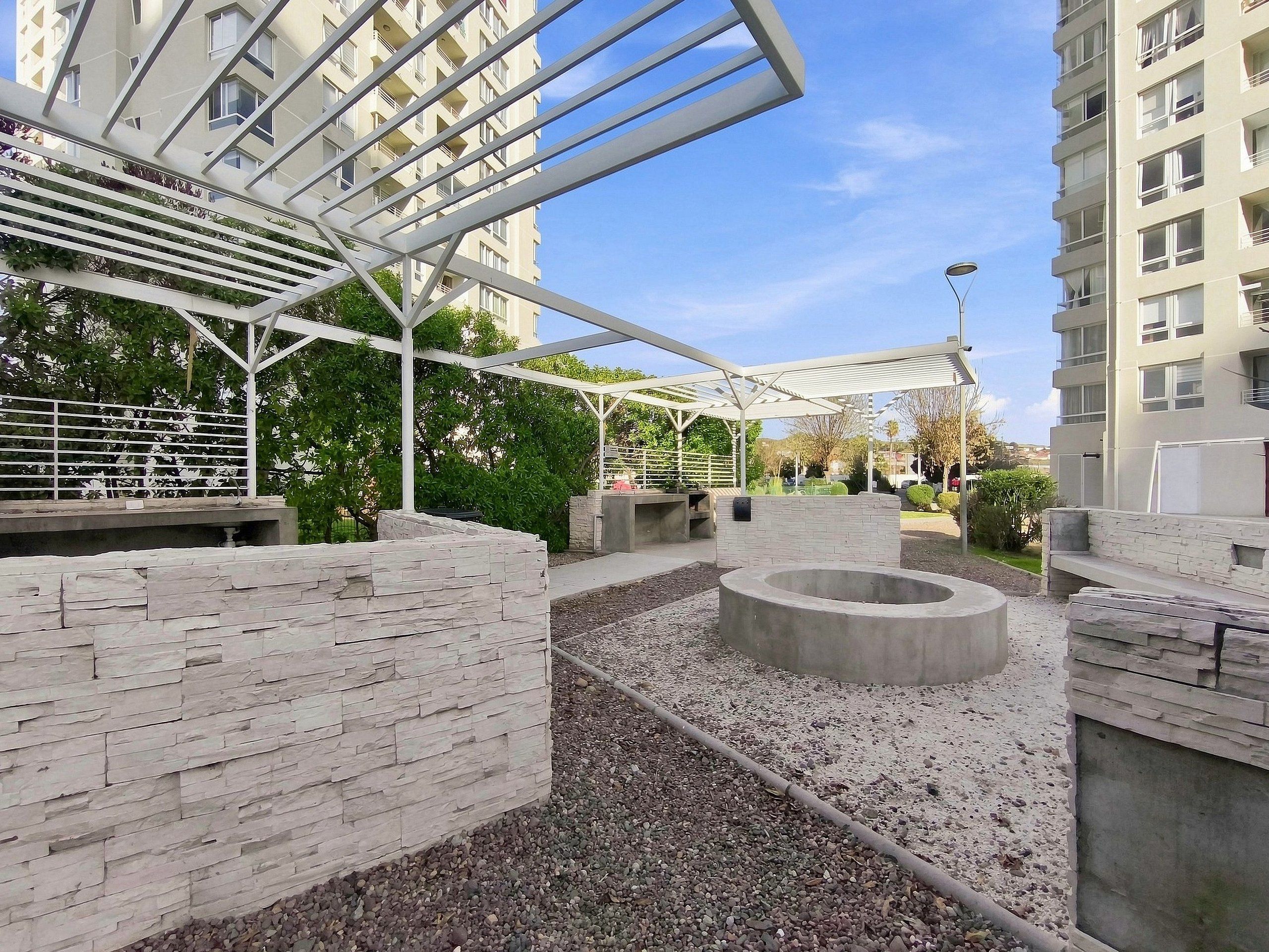 Ein moderner Außenbereich mit einer Steinwand, einer runden Sitzgruppe aus Beton und einer Pergola aus Metall.