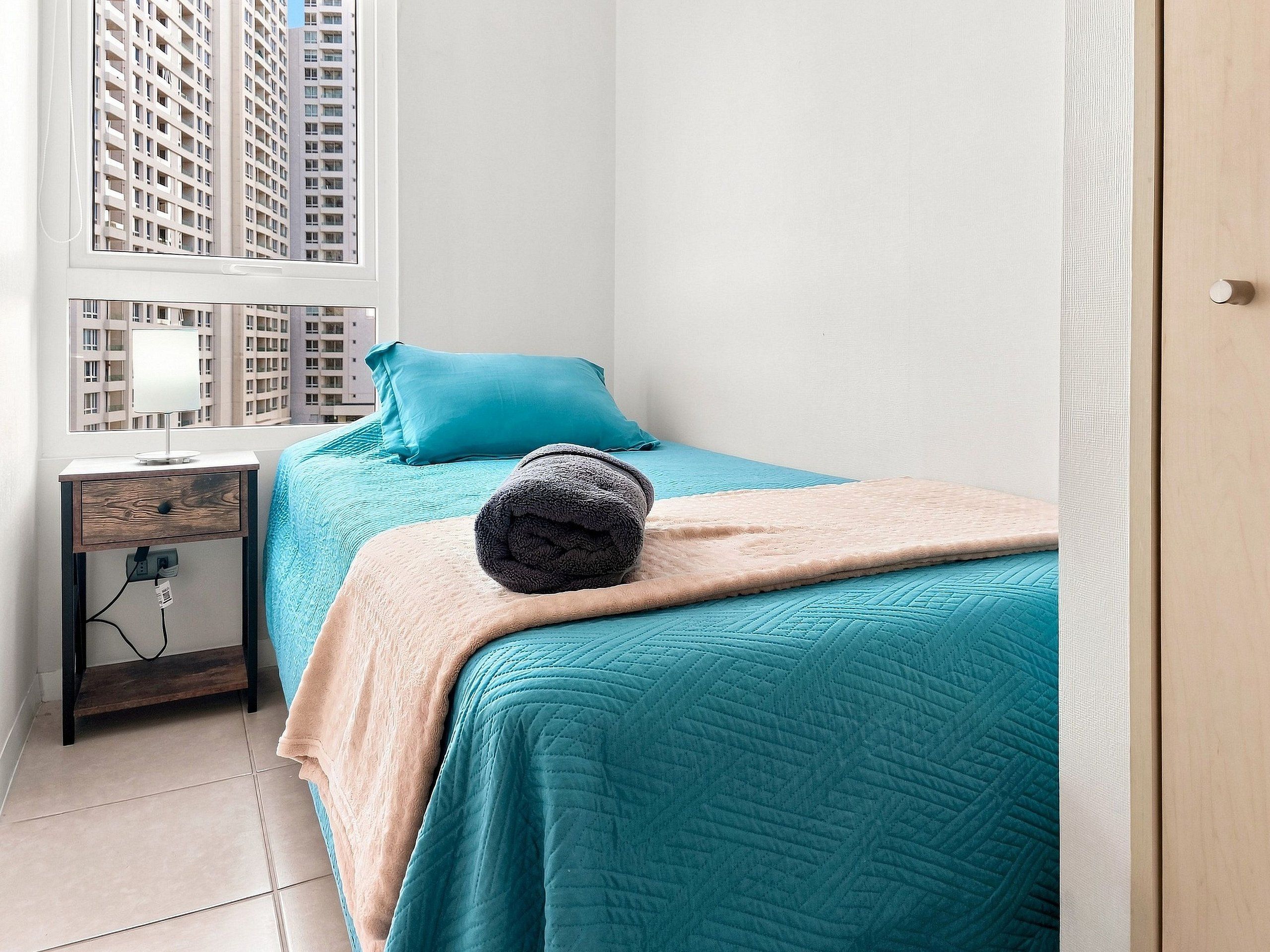 Una camera da letto con un letto, un comodino, una lampada e una finestra vista edifici.
