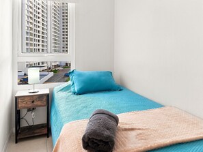 A small, neatly arranged bedroom with a bed, a bedside table, a lamp, and a window offering a view of a building. - Oceana Suites La Serena Peñuelas (Coquimbo)