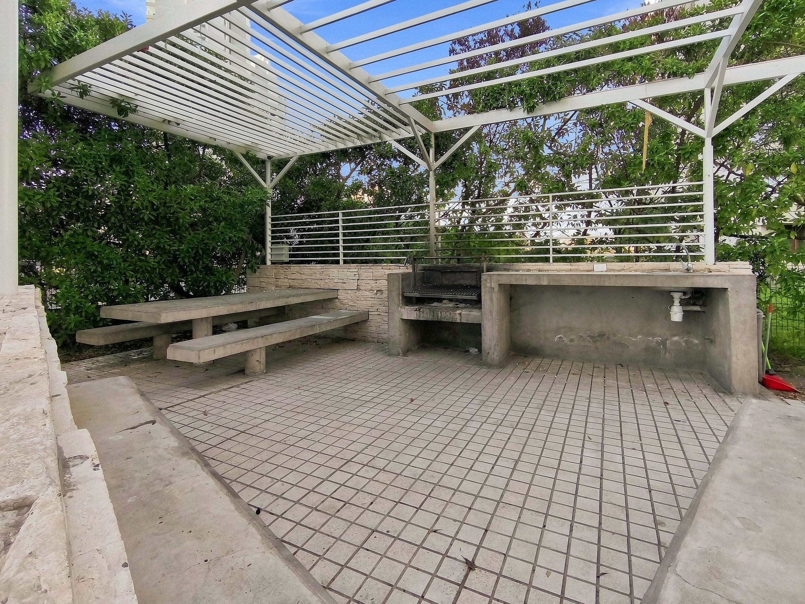 Um pátio externo com churrasqueira, área de estar e estrutura de pérgola.