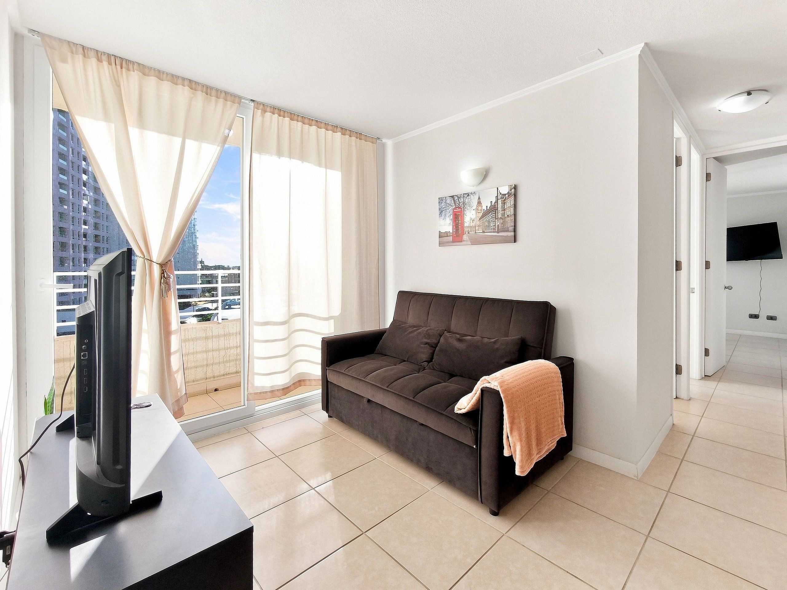 Sala de estar moderna com sofá, TV de tela plana e vista para a cidade através de grandes janelas.