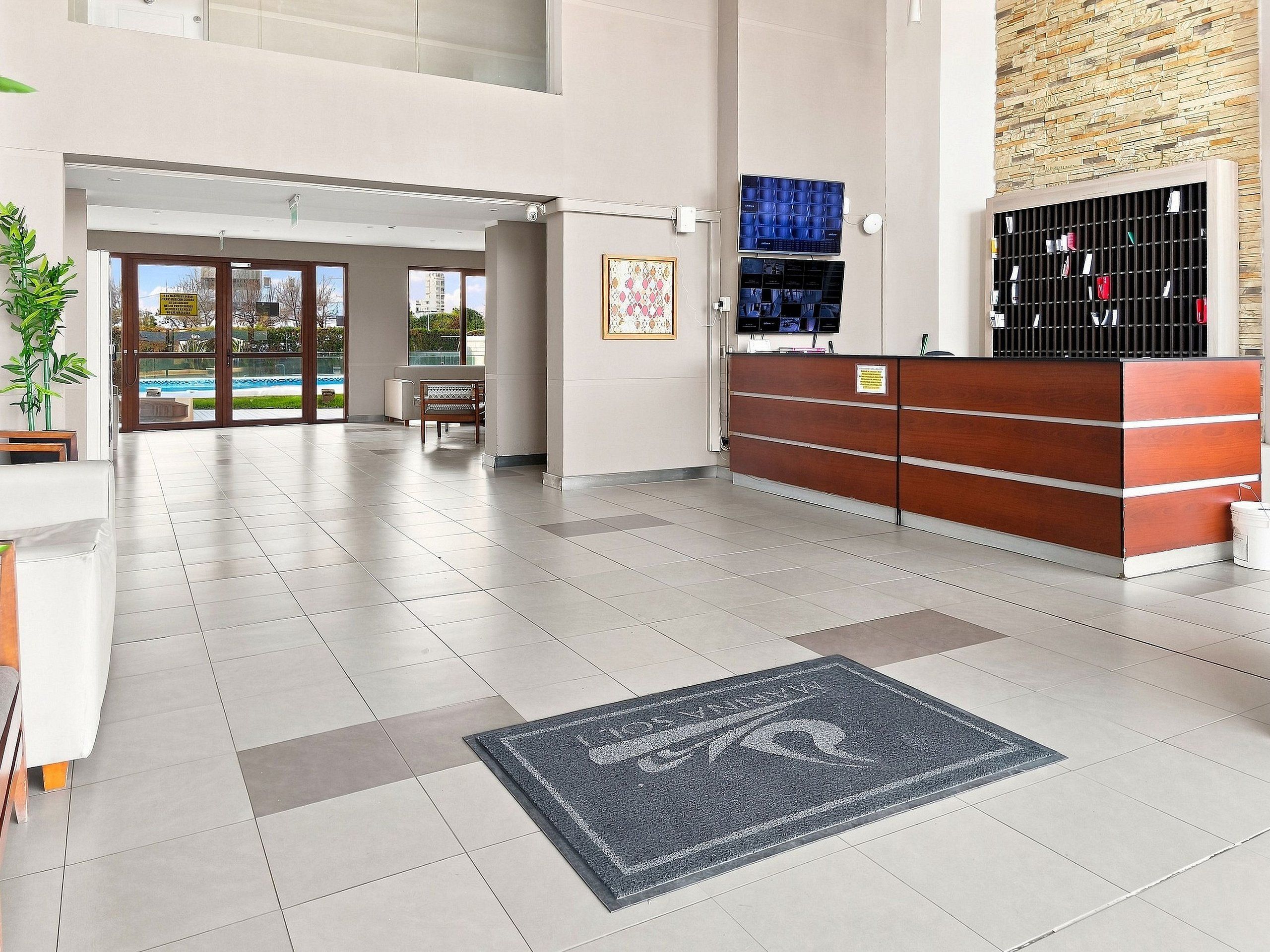 A reception area with a reception desk, a bench, and a view of a swimming pool through the glass doors.