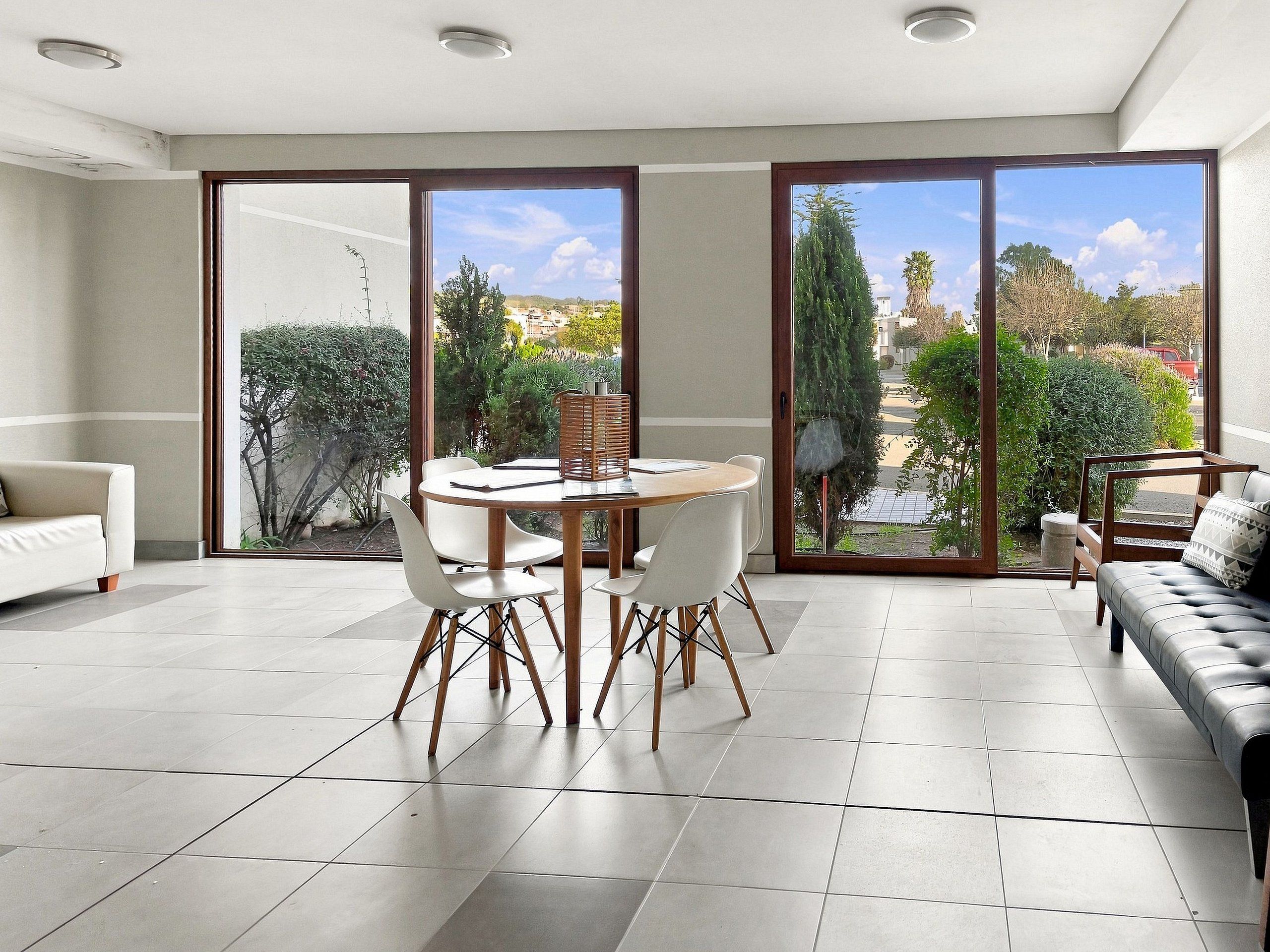 Uma sala de estar moderna com área de jantar, grandes portas de vidro deslizantes e vista para um jardim e prédios.
