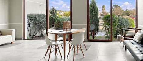 A modern living room with a dining area, large sliding glass doors, and a view of a garden and buildings.
