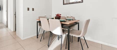 A dining area with a table set for two, chairs, a hanging light fixture, and a wall-mounted mirror.