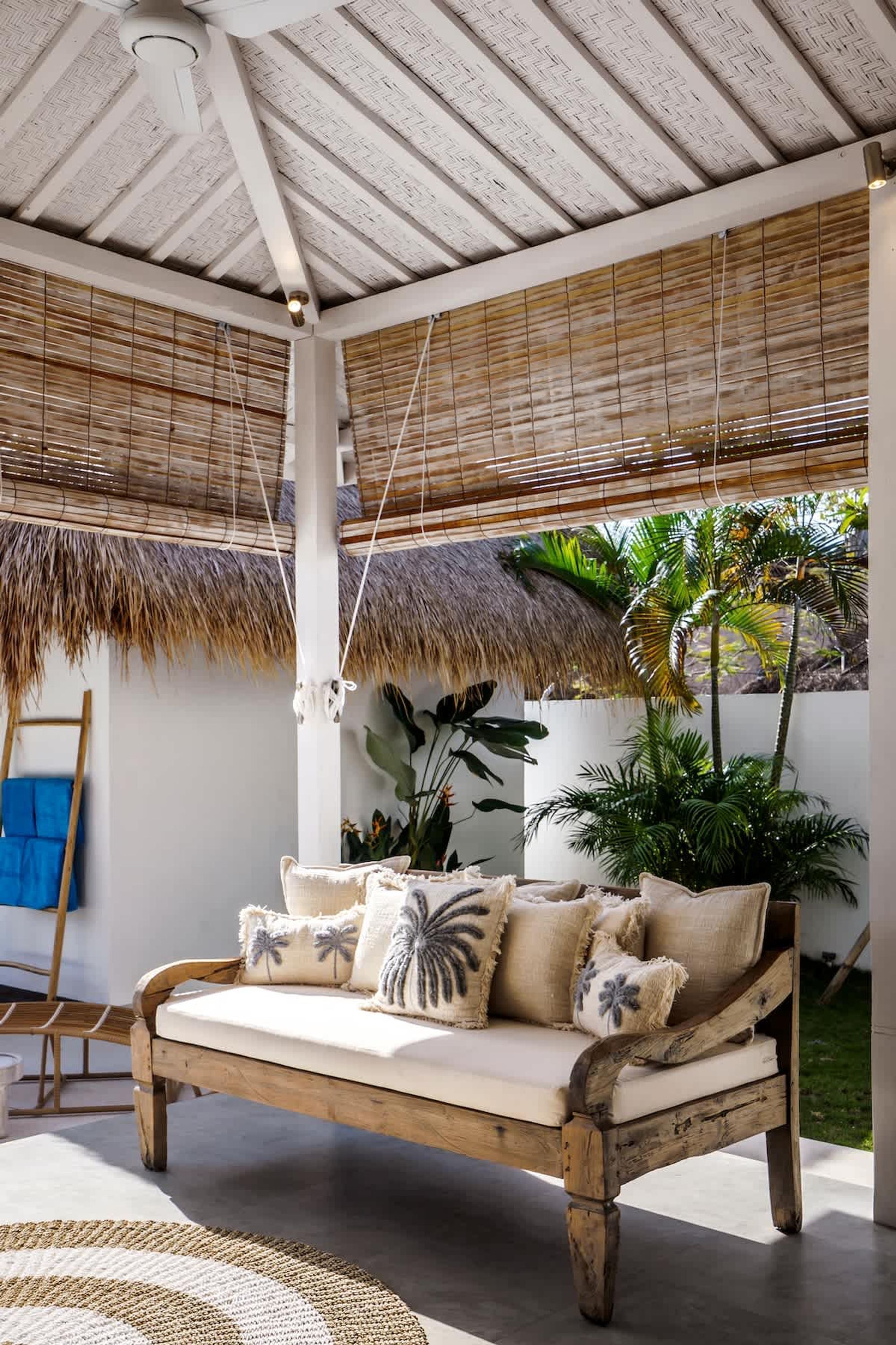 Un espace extérieur accueillant, avec un banc en bois, un toit de chaume et des plantes tropicales.