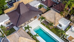 An aerial view of a resort with a swimming pool, thatched-roof structures, and palm trees. - Villa Surga Blue in Seminyak (Seminyak)
