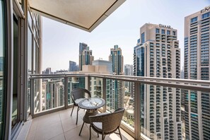 A balcony with a glass table and wicker chairs, overlooking a cityscape with high-rise buildings. - Cozy 1BR | Steps from Burj Khalifa & Mall (Dubai)