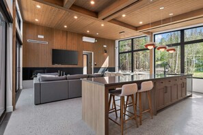 A modern kitchen with a large island, bar stools, and a built-in TV. - Spa & Direct lake access | Le Baska (Ferme-Neuve)