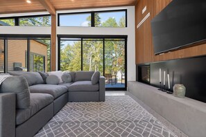 A modern living room with a sectional sofa, a patterned rug, and a large flat-screen TV mounted on the wall.