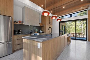 A modern kitchen with a central island, wooden cabinets, stainless steel appliances, and pendant lighting.
