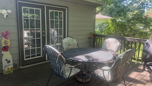 A covered patio with a round table and chairs, a door with a butterfly decoration, and a view of greenery.