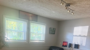 A room with a black leather chair, wooden flooring, a ceiling fan, and two windows with blinds.