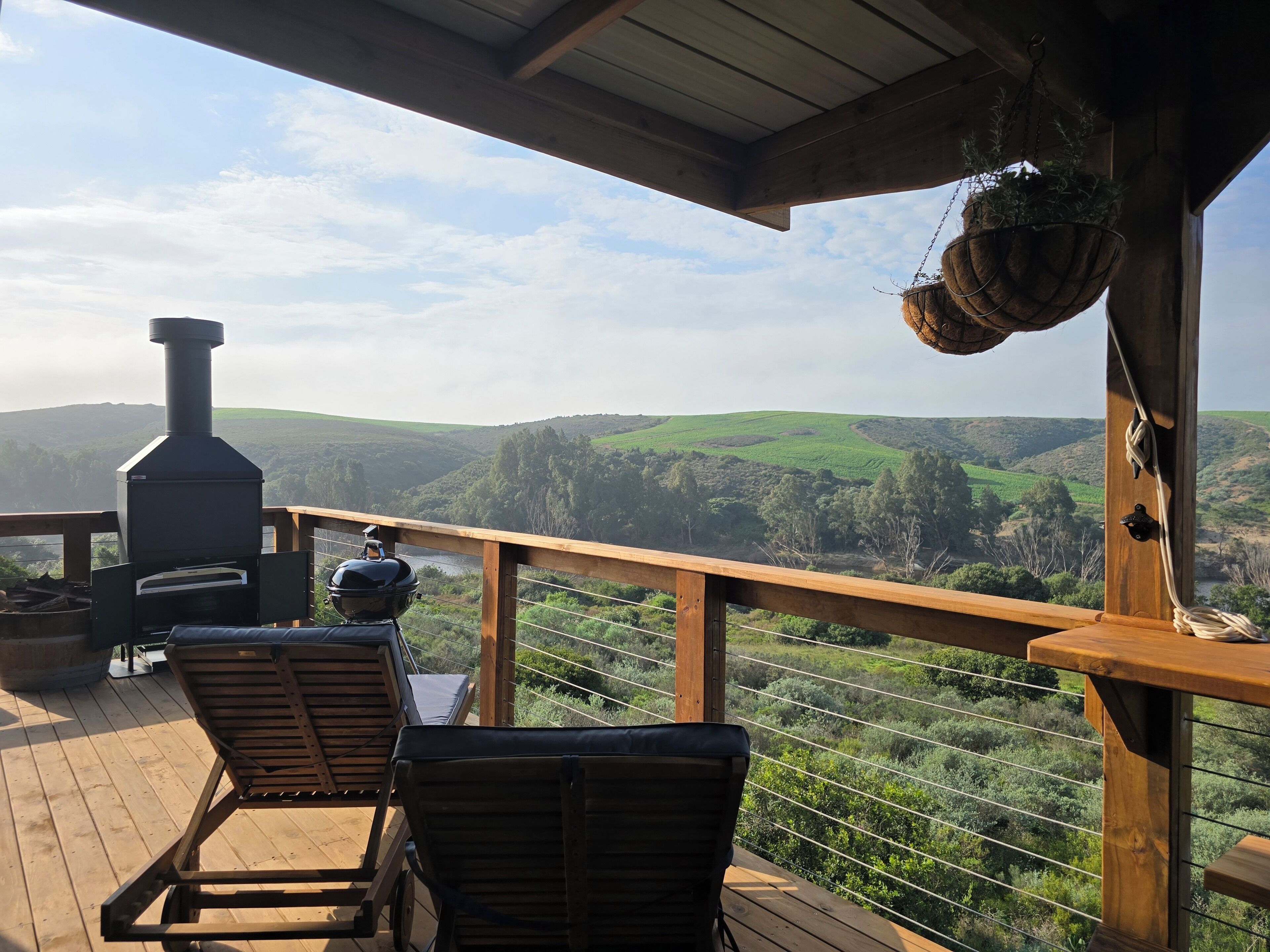 Una terraza de madera con una parrilla y sillones de descanso con vistas a un paisaje montañoso.
