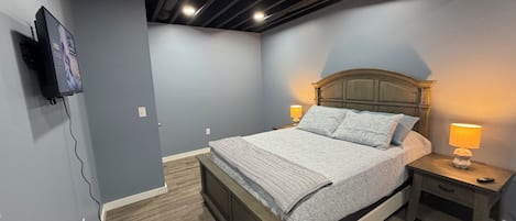 A bedroom with a bed, bedside tables, a TV mounted on the wall, and a ceiling with exposed beams.