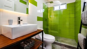 A modern bathroom with a white sink, a glass shower enclosure, and green tiled walls.