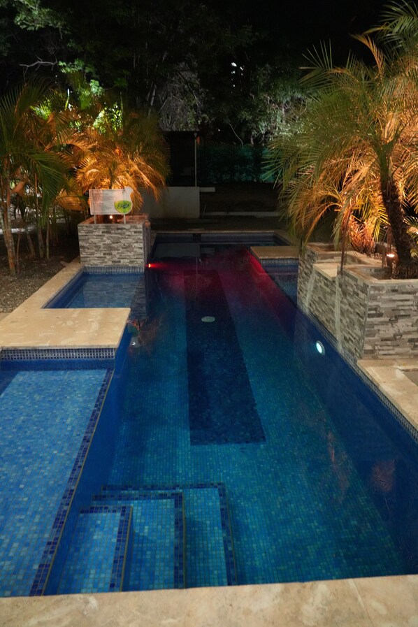 A swimming pool with a tiled floor, surrounded by stone walls and palm trees.