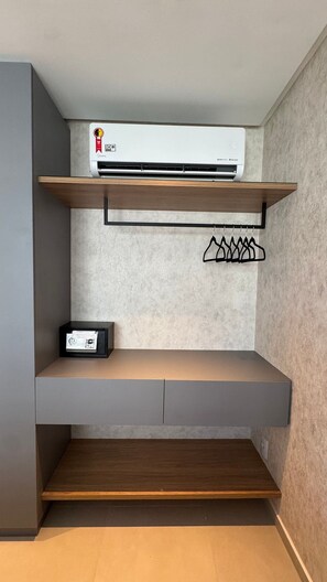 Une pièce dotée d’un système de climatisation intégré, d’une étagère avec un porte-vêtements suspendu et d’un petit appareil électronique placé sur une étagère inférieure.