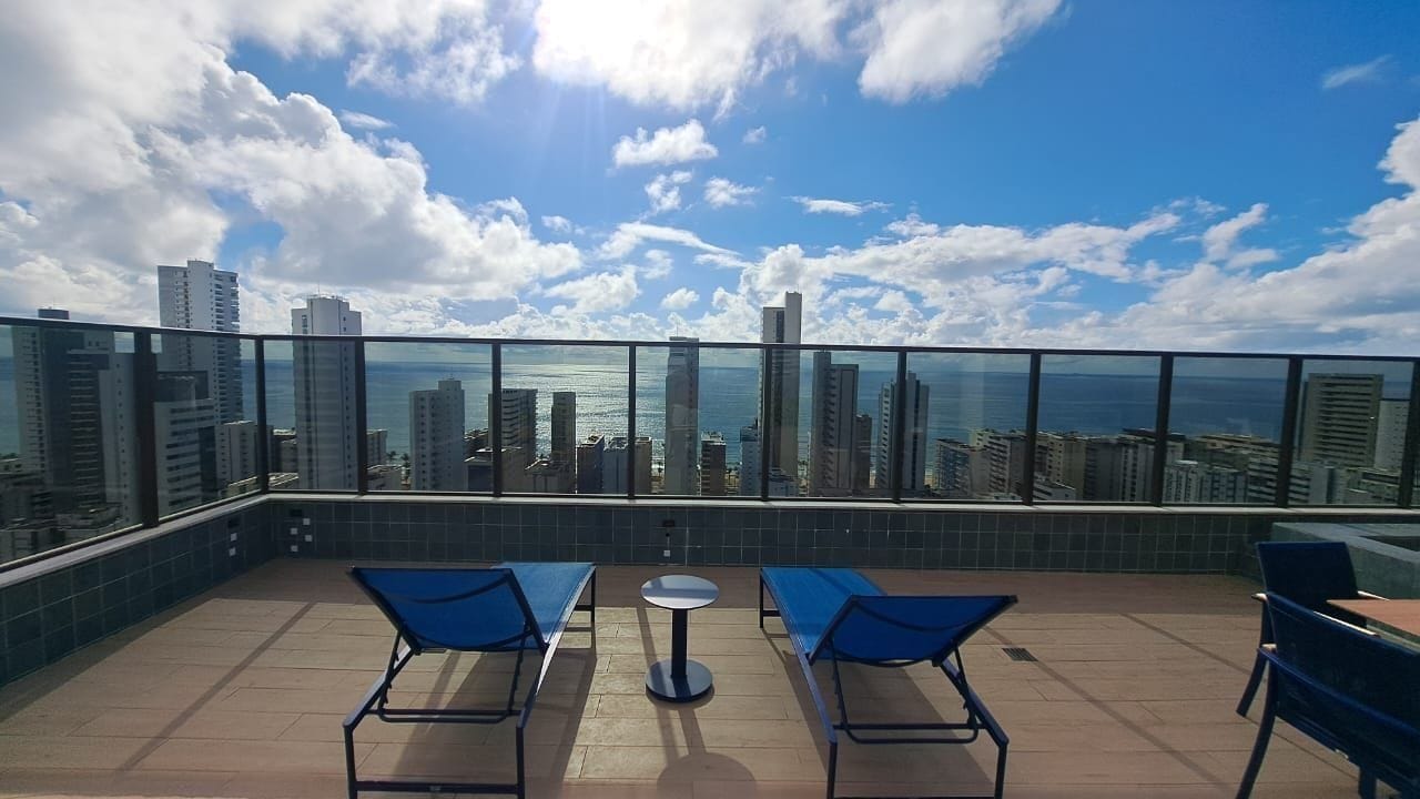 Terraza en la azotea con balaustrada de cristal, dos sillones azules, una mesa redonda y vistas al horizonte de la ciudad.