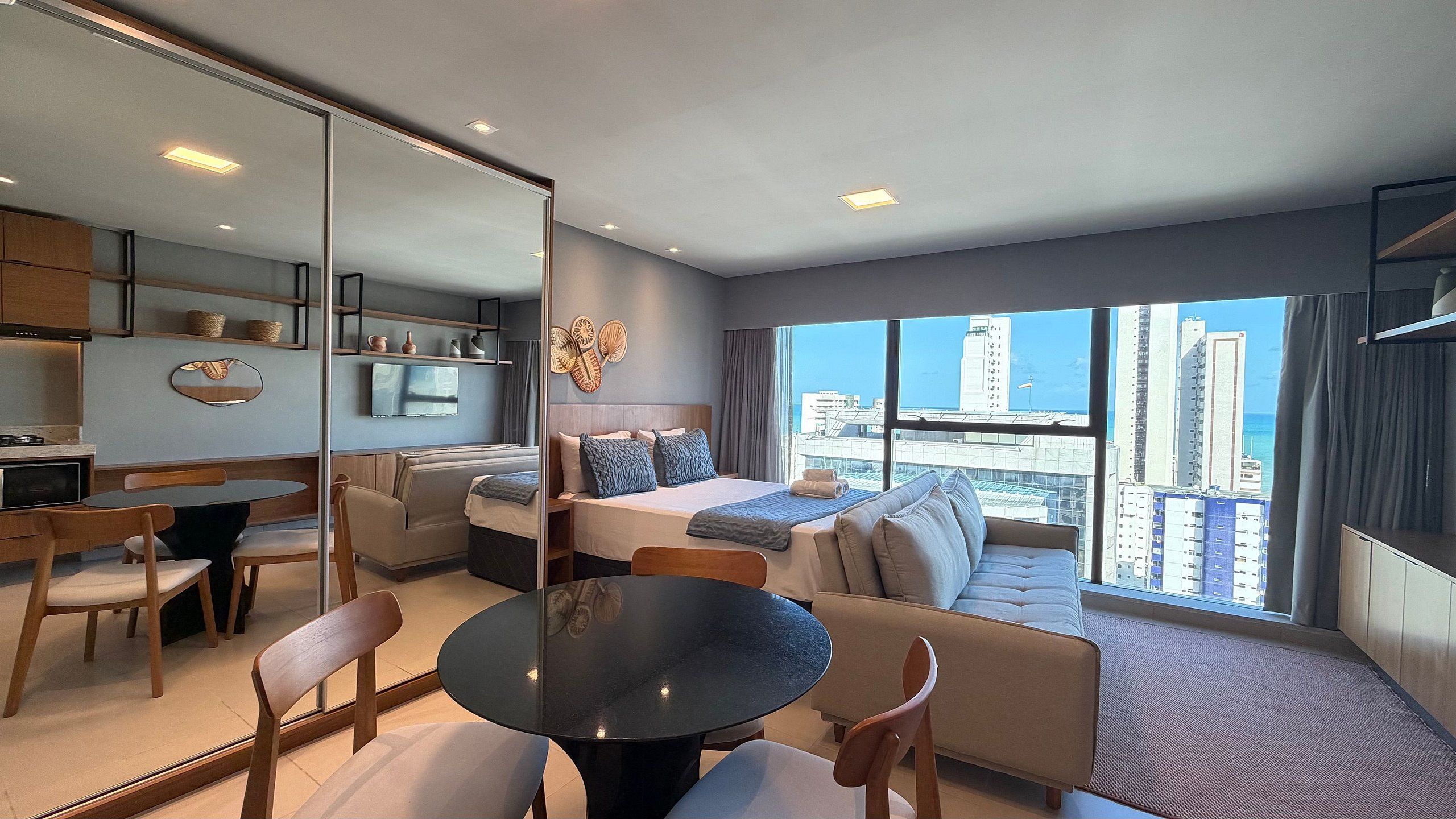 Habitación de hotel moderna con comedor, un sofá, una cama con vistas y un ventanal grande.