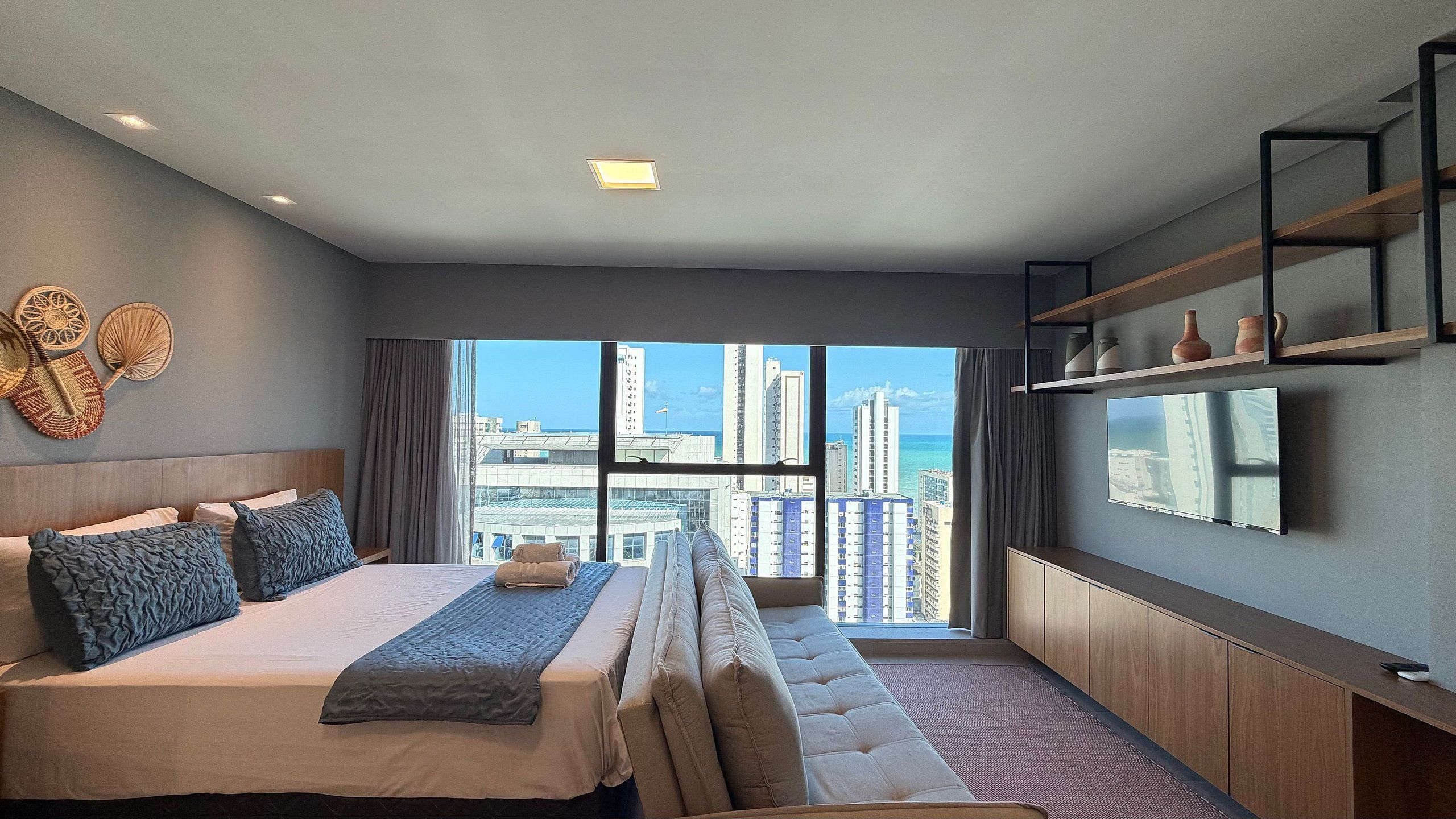 A modern hotel room with a large bed, a flat-screen TV, and a city view.