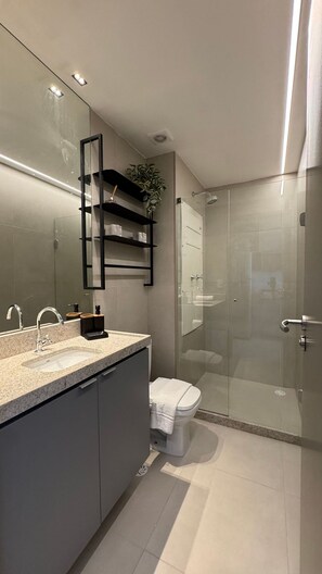 Ein modernes Badezimmer mit einer Duschkabine aus Glas, einem großen Spiegel und einer Arbeitsplatte aus Granit.